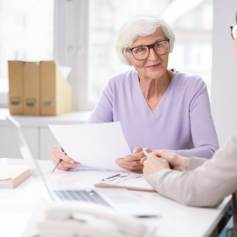 Content white-haired lady in glasses sitting at table and counseling on document issues with social worker